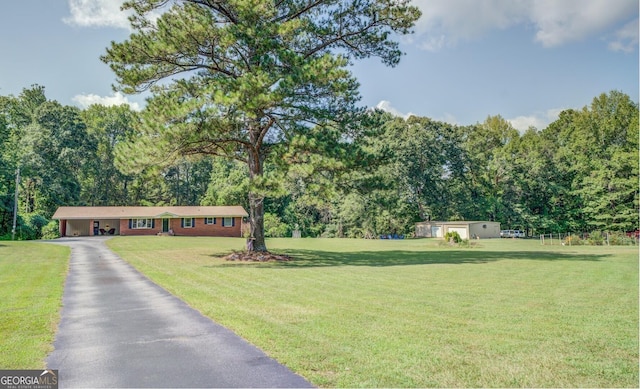 view of front of property featuring driveway, a garage, a forest view, an outdoor structure, and a front yard