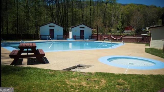 community pool featuring a community hot tub, an outdoor structure, a forest view, and a patio