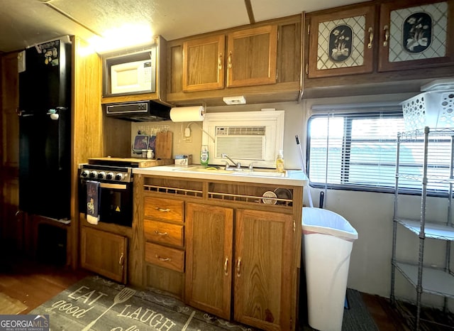 kitchen with white microwave, stainless steel gas range oven, under cabinet range hood, a sink, and brown cabinetry