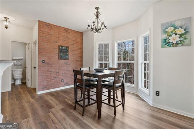 dining area featuring baseboards, a notable chandelier, brick wall, and wood finished floors