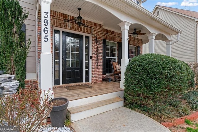 view of exterior entry with a porch, brick siding, and a ceiling fan