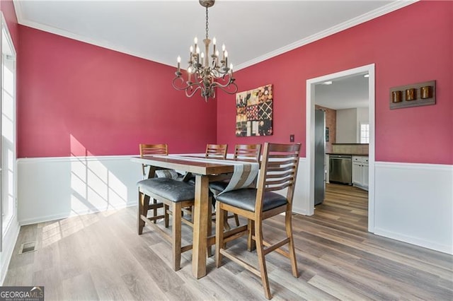 dining room featuring a chandelier, visible vents, crown molding, and wood finished floors