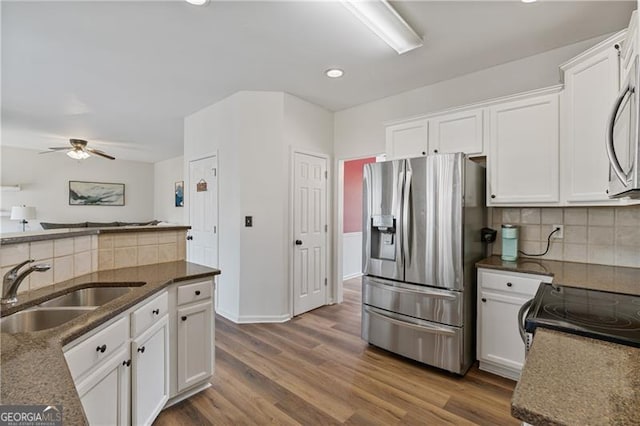 kitchen with stainless steel appliances, white cabinetry, a sink, dark stone countertops, and wood finished floors