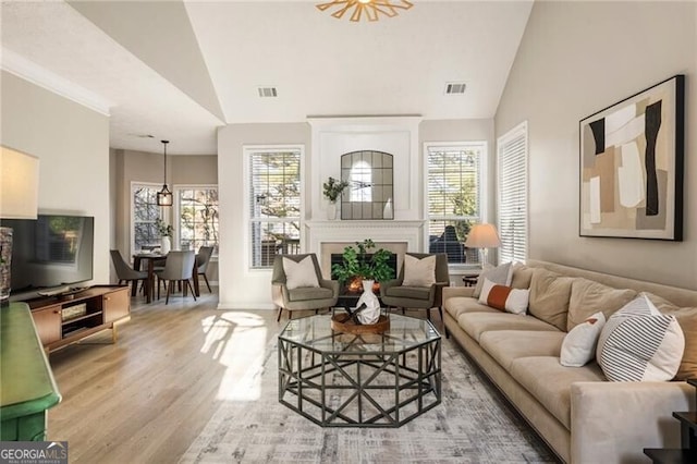 living area with lofted ceiling, a warm lit fireplace, visible vents, and light wood-style floors