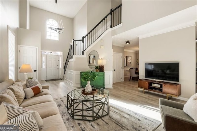 living room featuring light wood-style floors, a wainscoted wall, a high ceiling, and stairs