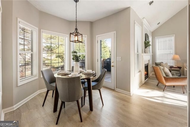 dining room with a warm lit fireplace, light wood-type flooring, visible vents, and a healthy amount of sunlight