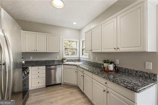 kitchen featuring stainless steel appliances, light wood finished floors, a sink, and white cabinetry