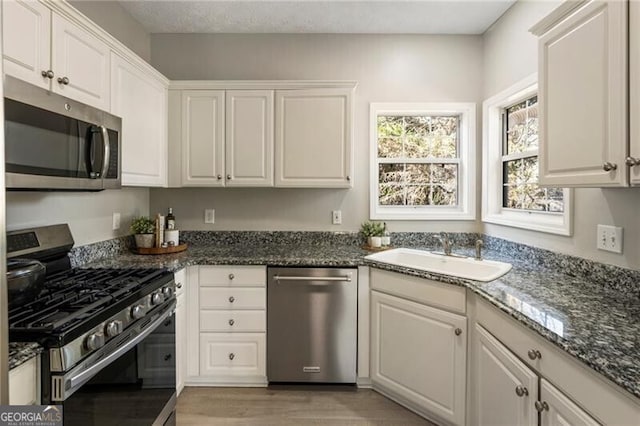 kitchen featuring appliances with stainless steel finishes, dark stone counters, white cabinetry, and a sink