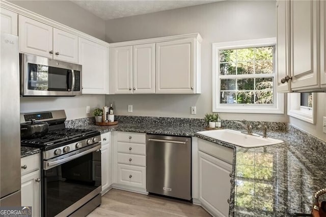 kitchen featuring light wood finished floors, appliances with stainless steel finishes, white cabinets, a sink, and a textured ceiling