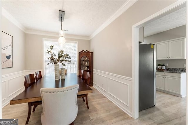 dining area with light wood-style flooring, ornamental molding, and a textured ceiling