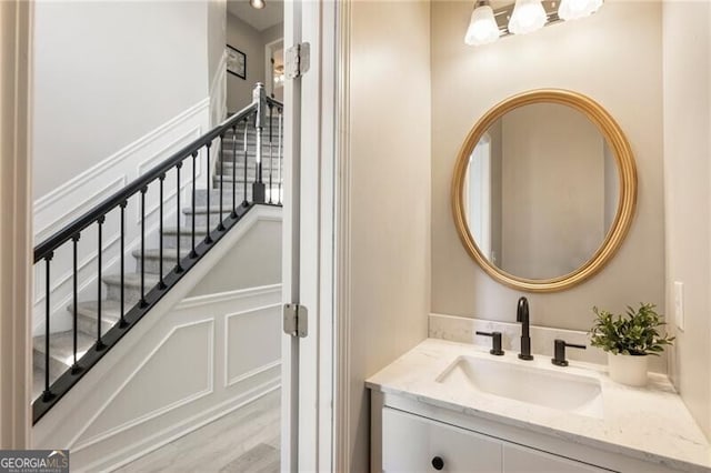 bathroom with a decorative wall, vanity, and wood finished floors