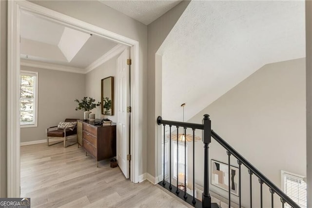 hallway with baseboards, lofted ceiling, light wood-style flooring, crown molding, and an upstairs landing