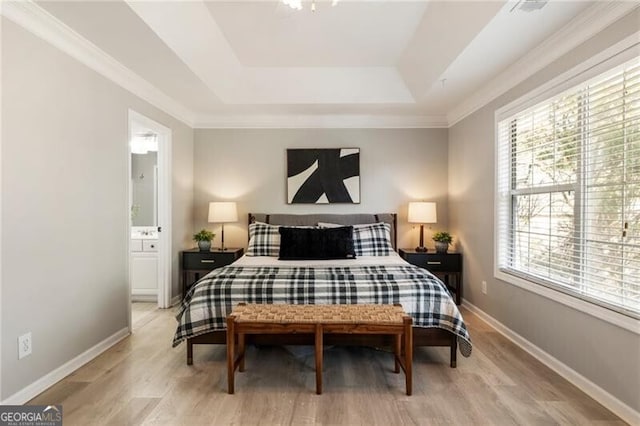 bedroom featuring light wood-style floors, a tray ceiling, ensuite bath, and baseboards