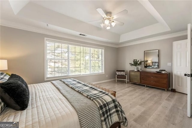 bedroom with visible vents, baseboards, ornamental molding, a tray ceiling, and light wood-style floors