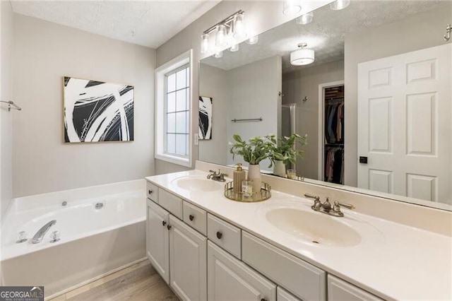 full bath featuring a textured ceiling, double vanity, a sink, and a bath