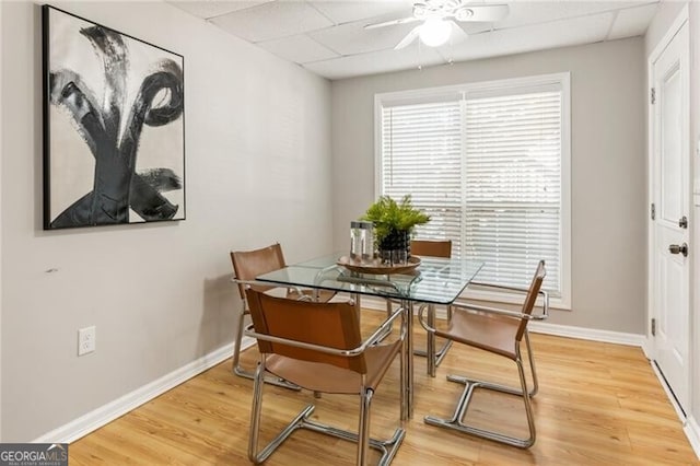 dining area with baseboards, a drop ceiling, and light wood finished floors