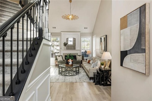 entrance foyer with a warm lit fireplace, high vaulted ceiling, wood finished floors, visible vents, and stairway