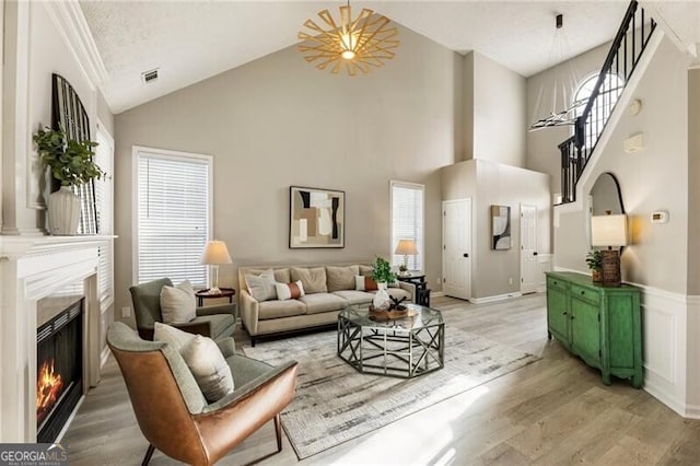 living area with high vaulted ceiling, visible vents, stairway, light wood-type flooring, and a glass covered fireplace