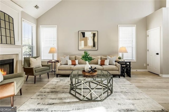 sitting room with high vaulted ceiling, visible vents, baseboards, a lit fireplace, and light wood finished floors