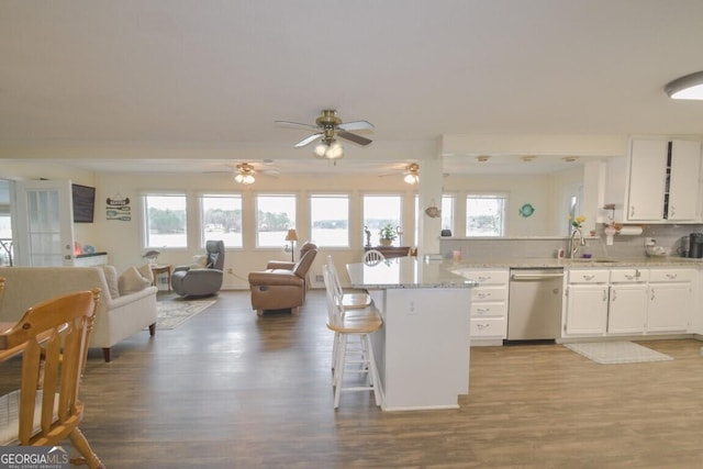 kitchen with a kitchen bar, a peninsula, wood finished floors, white cabinetry, and stainless steel dishwasher