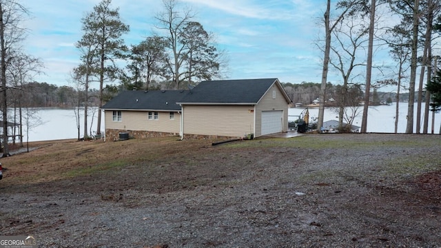 exterior space featuring central AC unit, driveway, a garage, and a water view