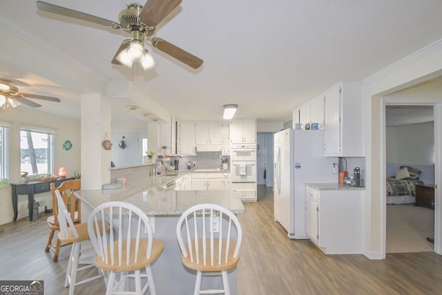 kitchen with a peninsula, freestanding refrigerator, light wood-style floors, white cabinetry, and a sink