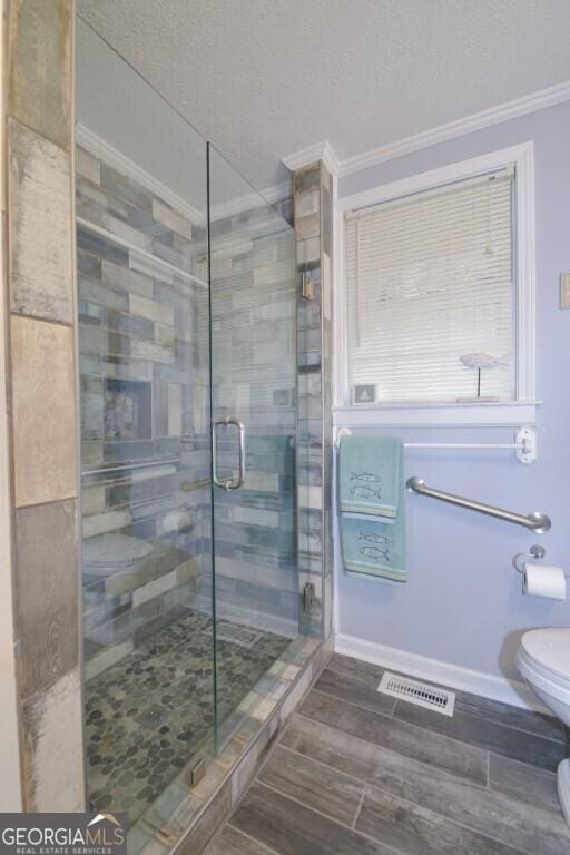 bathroom featuring visible vents, toilet, wood finished floors, a shower stall, and crown molding