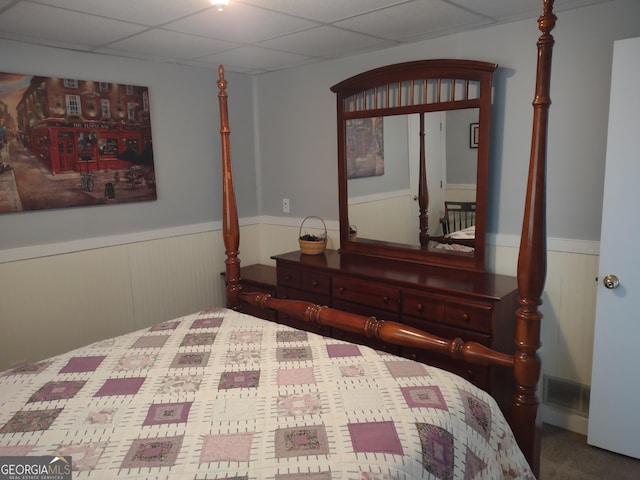 bedroom featuring a wainscoted wall, visible vents, and a drop ceiling