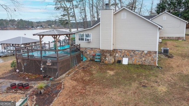 view of side of property with central AC unit, a deck with water view, a yard, a chimney, and a gazebo