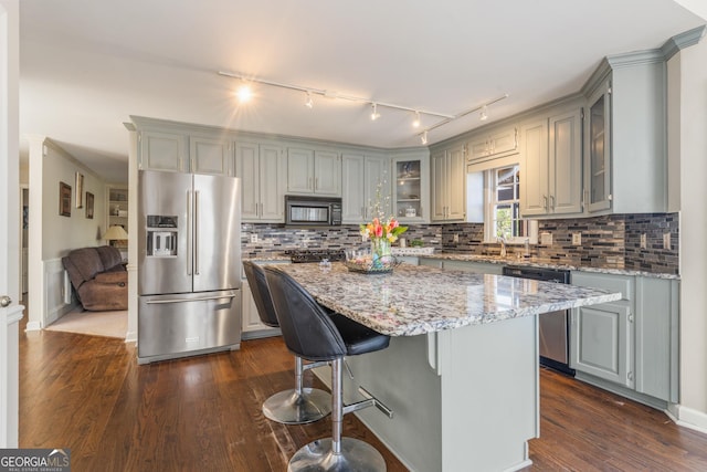 kitchen with gray cabinets, dark wood-type flooring, glass insert cabinets, appliances with stainless steel finishes, and a center island