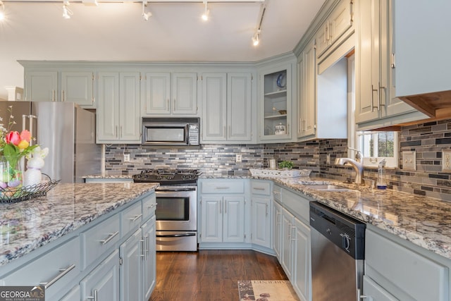 kitchen featuring dark wood-style floors, light stone countertops, a sink, stainless steel appliances, and backsplash