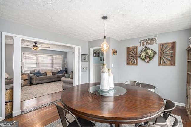 dining room featuring a ceiling fan, baseboards, wood finished floors, a textured ceiling, and ornate columns