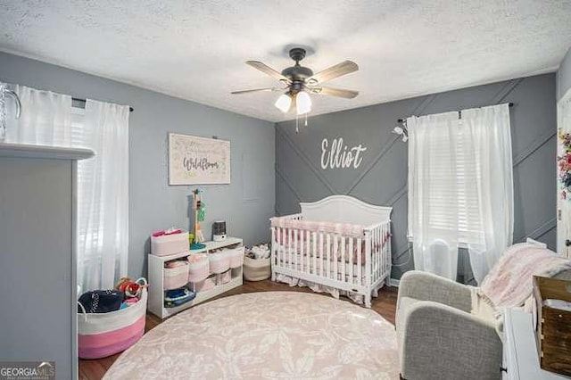 bedroom featuring a crib, wood finished floors, a ceiling fan, and a textured ceiling