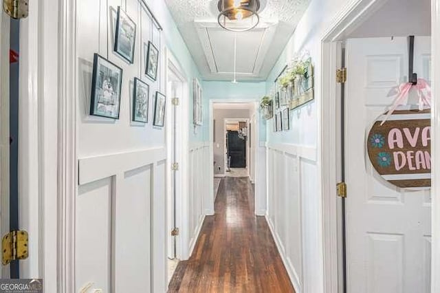 corridor featuring a decorative wall, attic access, dark wood-type flooring, and a wainscoted wall