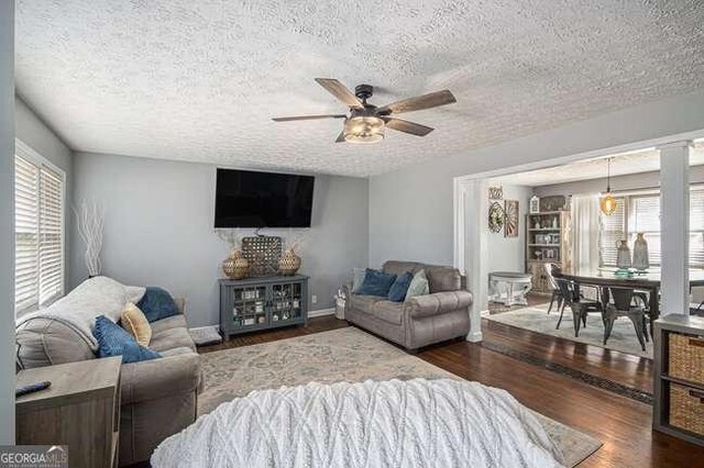 living room with baseboards, a textured ceiling, wood finished floors, and a ceiling fan