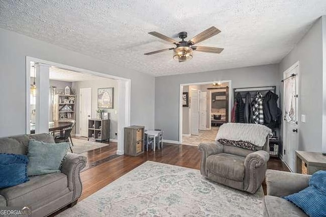 living area featuring baseboards, a textured ceiling, ceiling fan, and wood finished floors