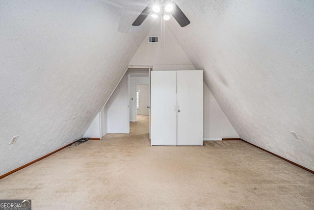 additional living space with visible vents, a textured ceiling, lofted ceiling, and carpet