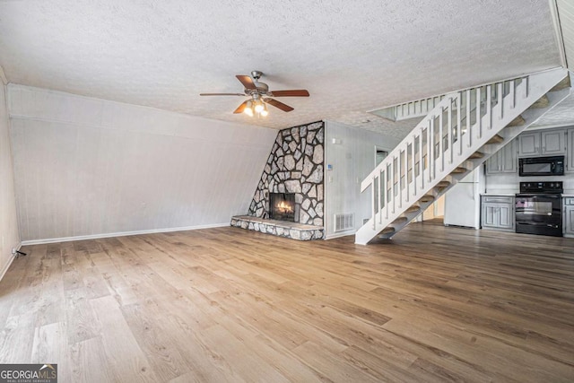 unfurnished living room with stairway, a fireplace, visible vents, and wood finished floors