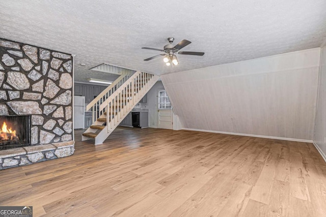 unfurnished living room with stairway, a textured ceiling, a stone fireplace, and wood finished floors