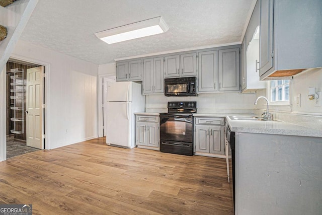 kitchen featuring gray cabinetry, light wood-type flooring, light countertops, black appliances, and a sink