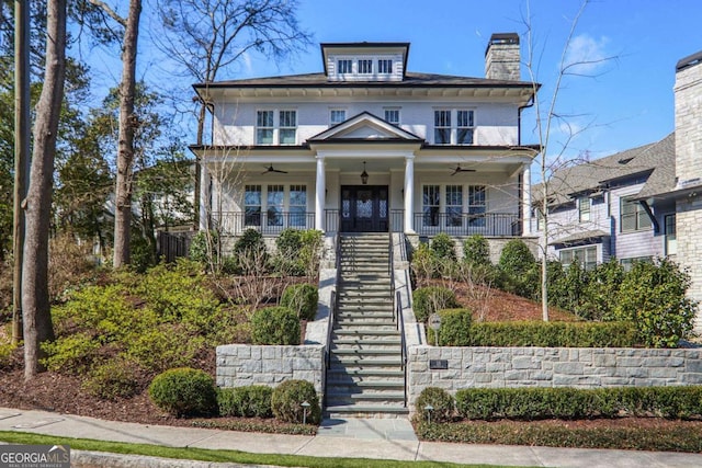 american foursquare style home featuring stairway, a porch, ceiling fan, and a chimney