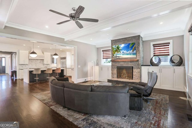 living area featuring beam ceiling, ornamental molding, dark wood-style floors, a stone fireplace, and baseboards