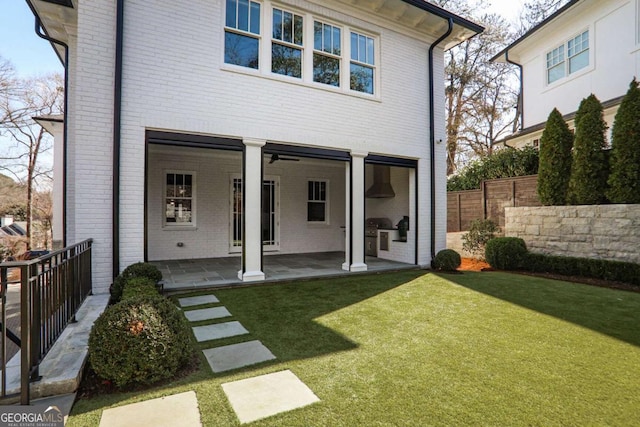 rear view of property featuring a yard, brick siding, a patio area, and fence