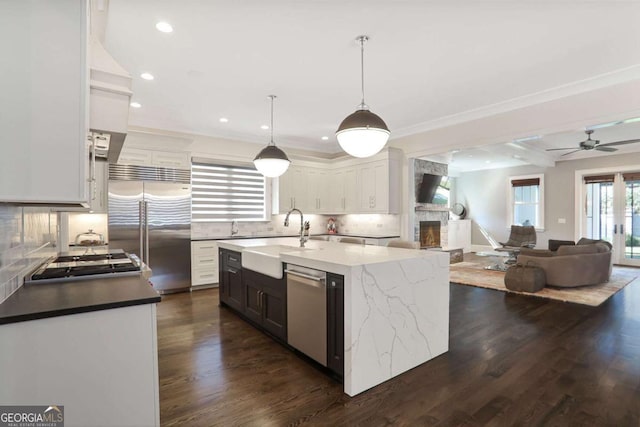 kitchen with a sink, stainless steel appliances, a large fireplace, and dark wood-style flooring