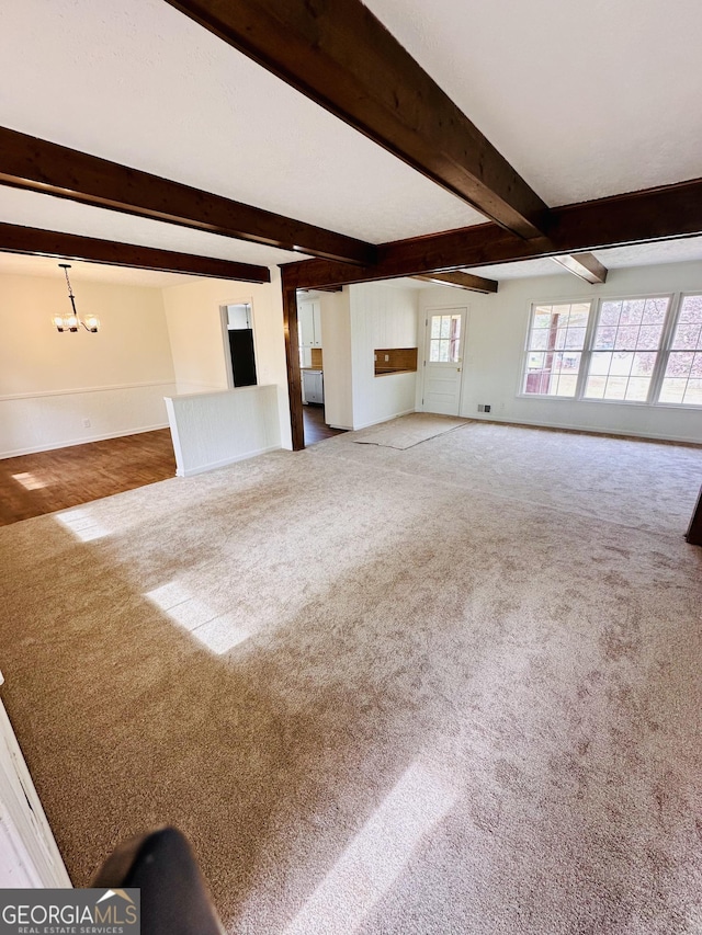 unfurnished living room with a chandelier, beamed ceiling, baseboards, and carpet