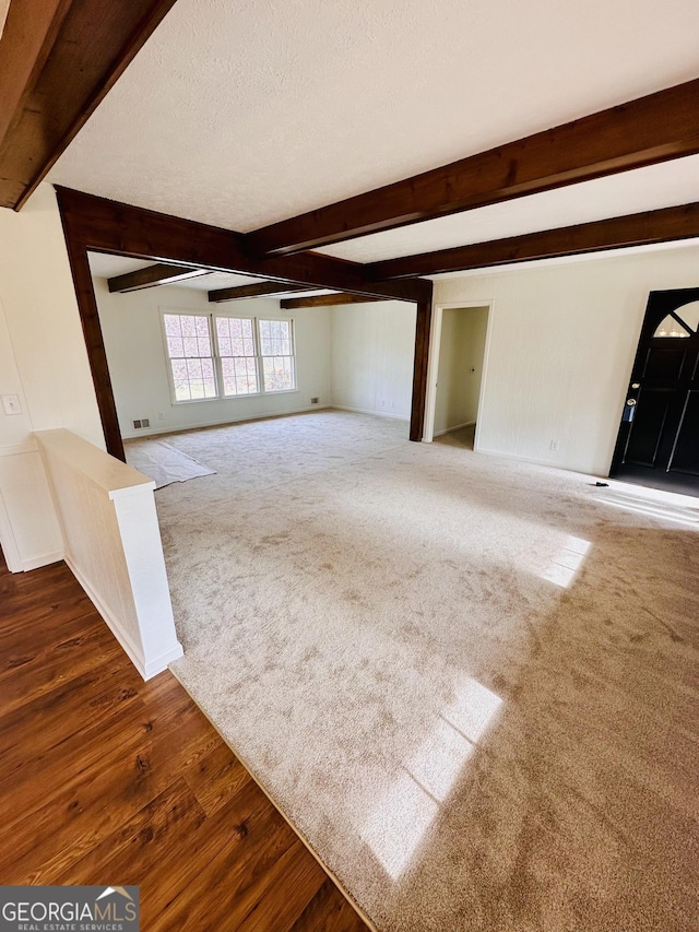 unfurnished living room featuring visible vents, beam ceiling, a textured ceiling, and dark carpet