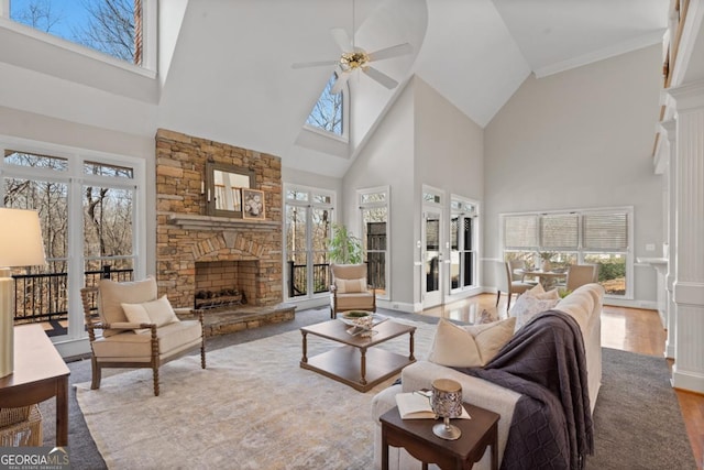 living area featuring a ceiling fan, wood finished floors, a high ceiling, a stone fireplace, and baseboards