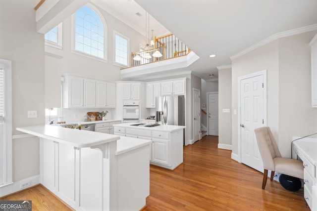 kitchen featuring a kitchen island, a peninsula, stainless steel appliances, light wood-style floors, and crown molding