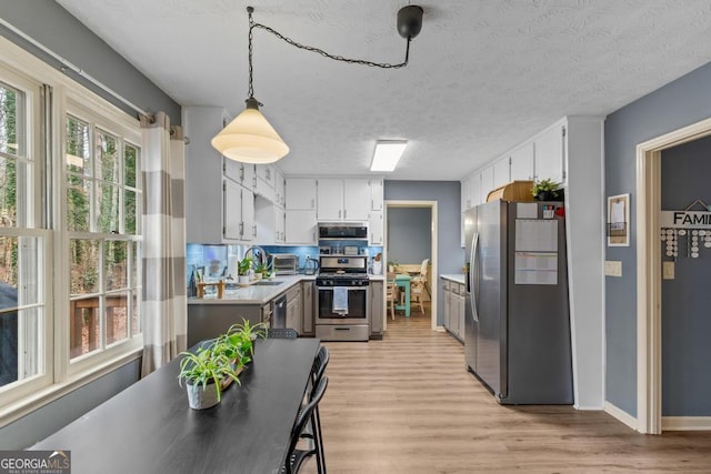 kitchen with light wood finished floors, light countertops, stainless steel appliances, white cabinets, and a textured ceiling