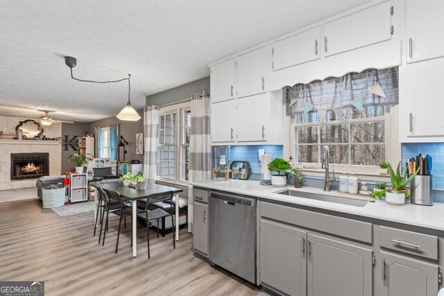 kitchen with a wealth of natural light, a sink, tasteful backsplash, stainless steel dishwasher, and a lit fireplace